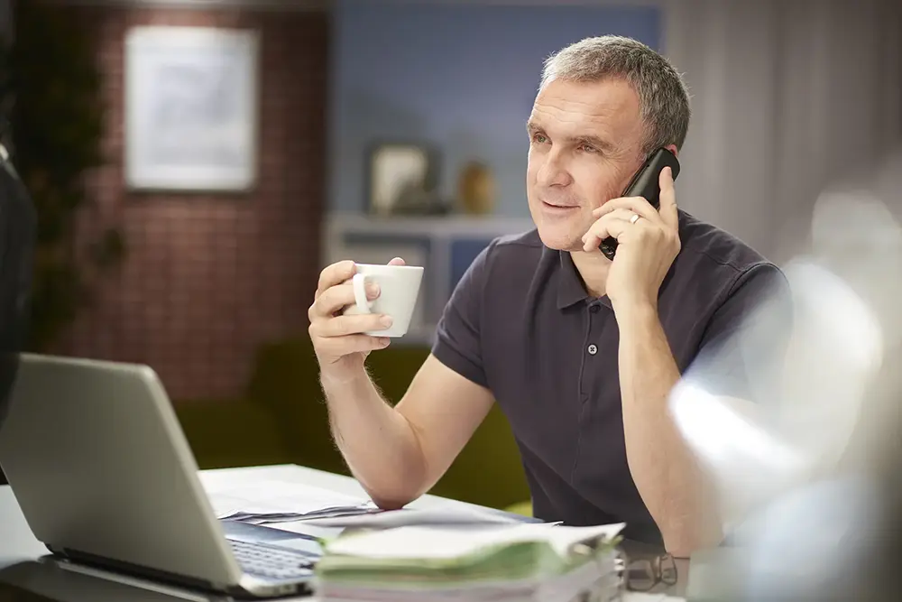 relaxed business owner with cup of coffee on the phone with the factoring company.