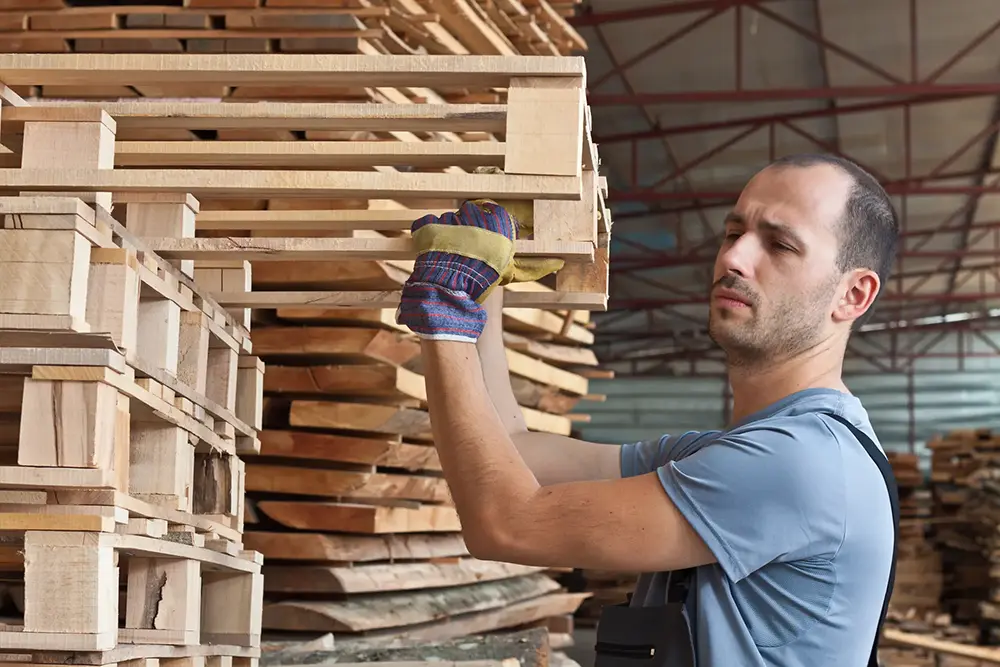 Man arranging wooden pallets in warehouse 